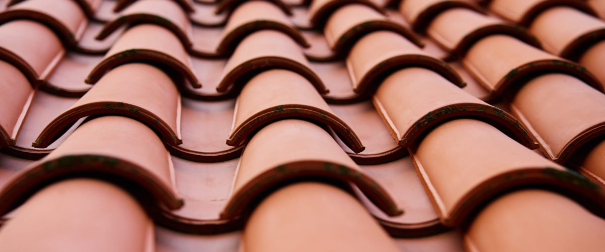Red ceramic roof tiles covering residential building roof. Tile pattern close-up